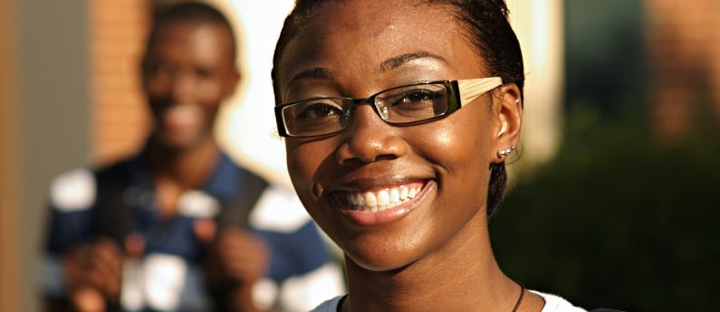 Close up of a smiling student, another student is out of focus in the background.