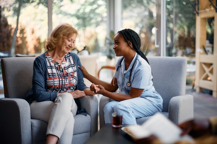 Smiling nurse sitting with patient and holding her hand